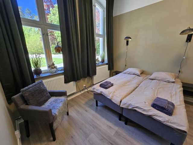 Rum med två bäddade sängar, fåtölj och utsikt mot grönskan